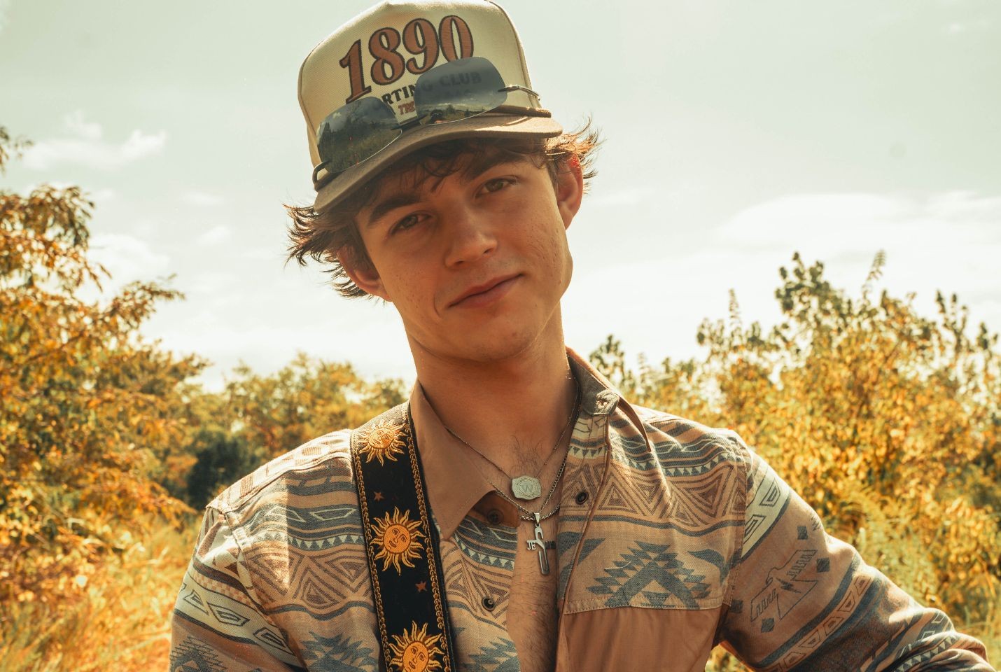 A man wearing a western printed shirt, cap, and sunglasses